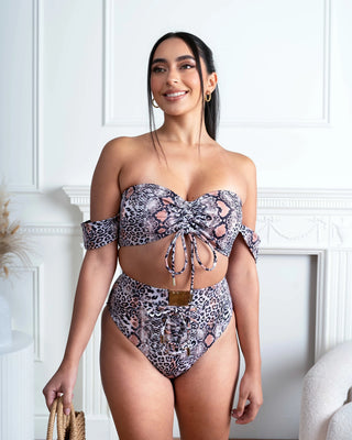 Woman wearing a leopard patterned bikini set in a room with white walls and decor.