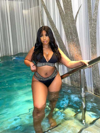Woman in a black bikini standing in a pool with decorative curtains in the background