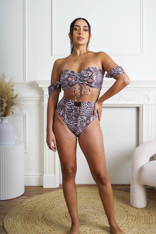 Woman wearing a leopard patterned bikini set in a room with white walls and a rug.