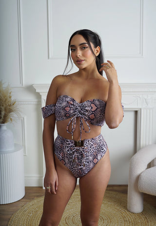 Woman wearing a leopard patterned bikini set in a room with white walls and a fireplace.