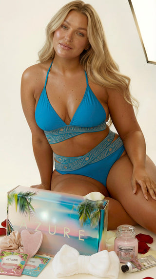Woman in blue bikini sitting next to an AZURE product box on a white background