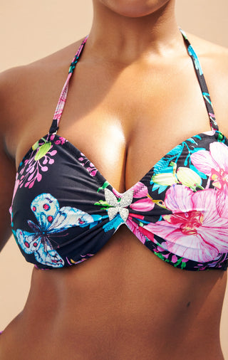 Colorful floral and butterfly bikini top on a person against a beige background